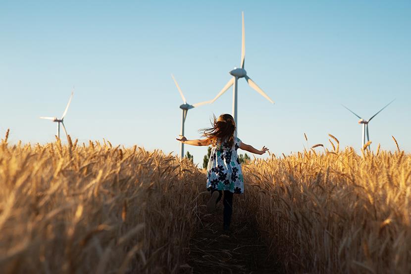 Girl running through field towards wind turbines