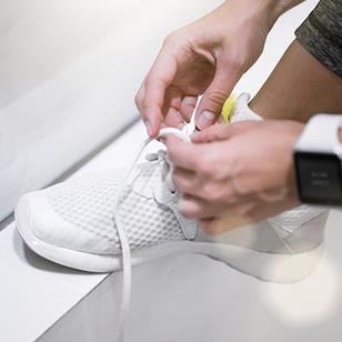 person wearing smartwatch tying laces of white sneaker